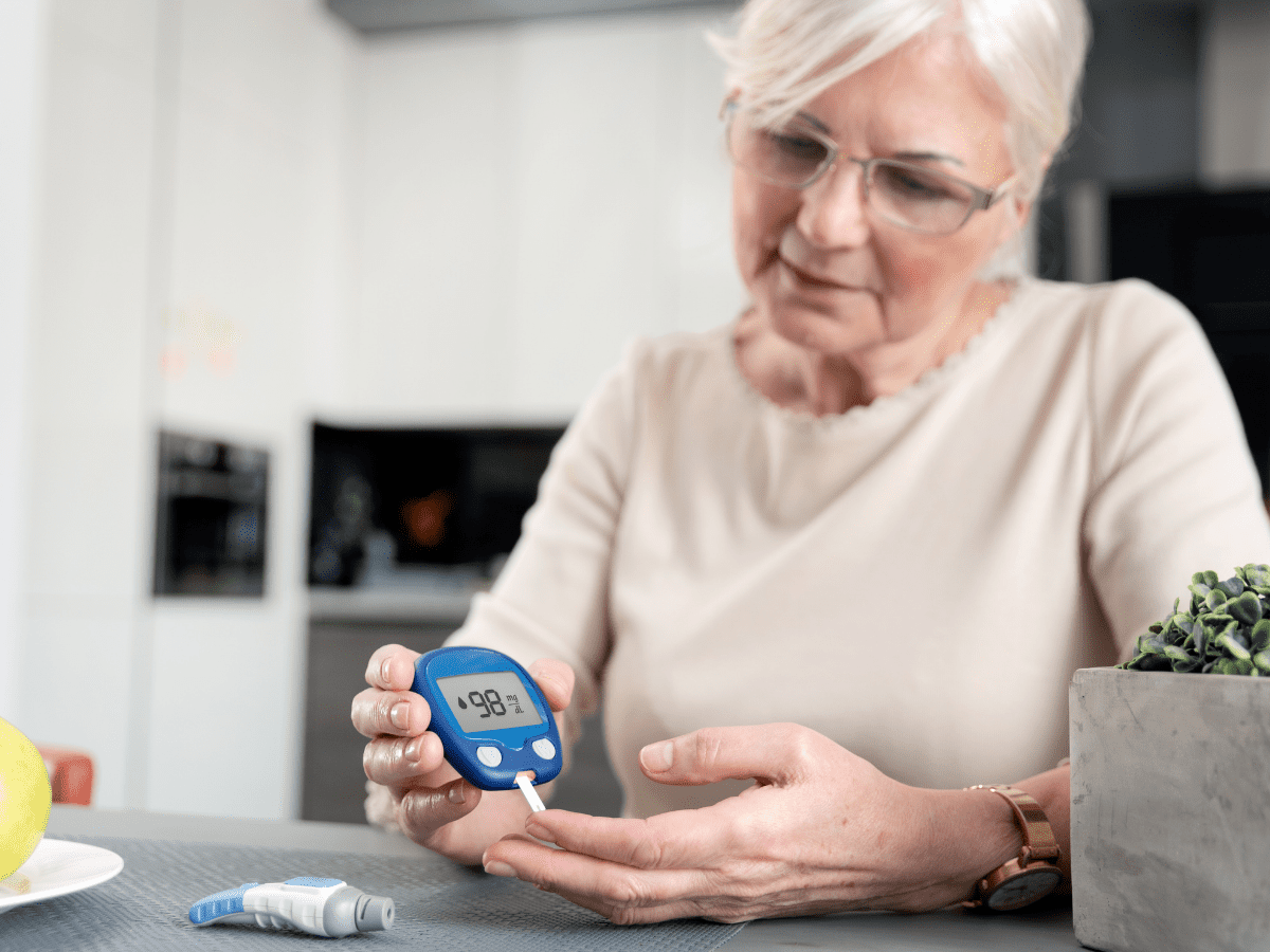 Woman sitting at table wearing eyeglasses testing blood sugar