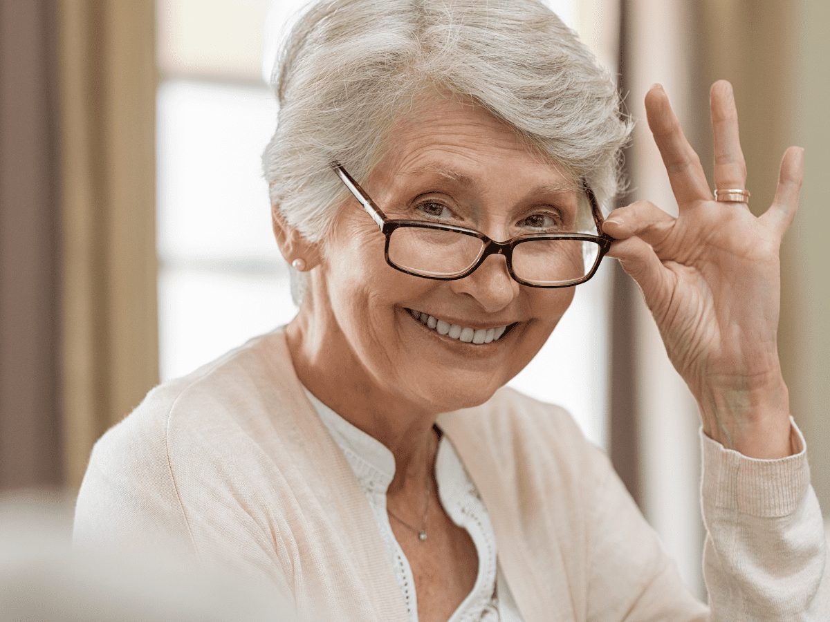 Smiling Woman with gray hair tipping her eyeglasses