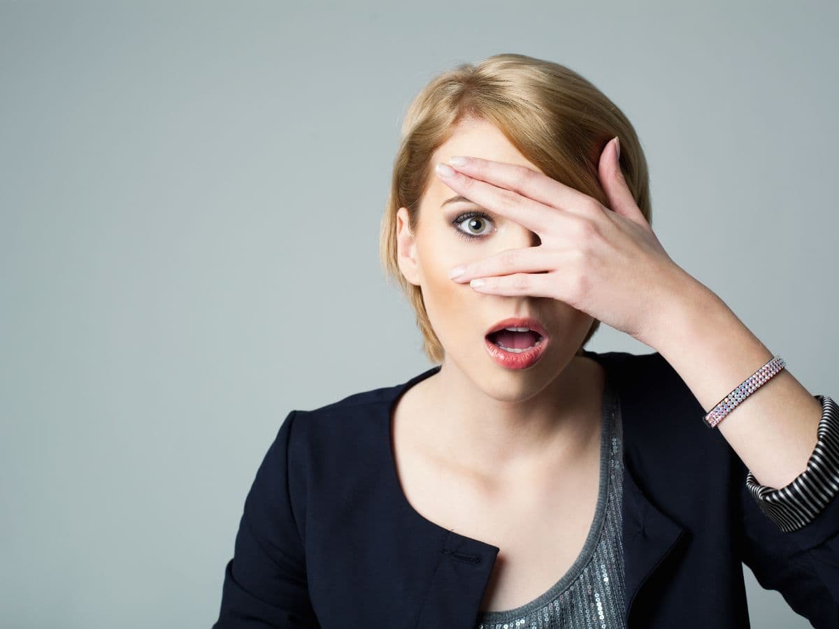 Woman looking through her fingers with her hand in front of her eye.