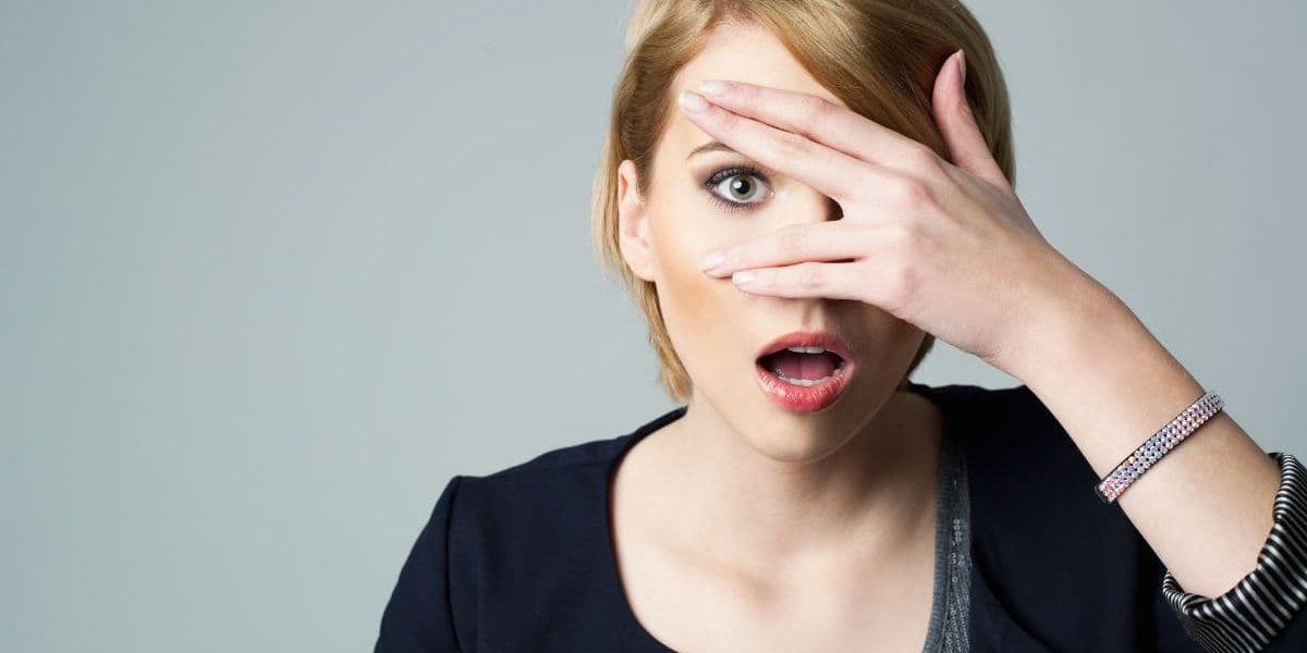 Woman looking through her fingers with her hand in front of her eye.