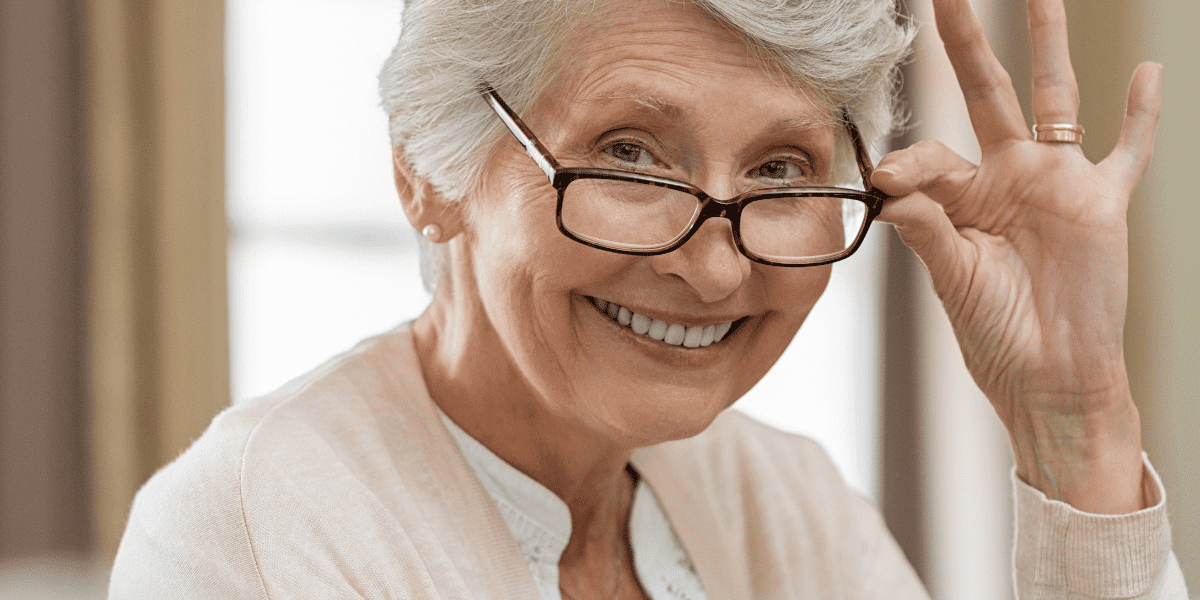 Smiling Woman with gray hair tipping her eyeglasses